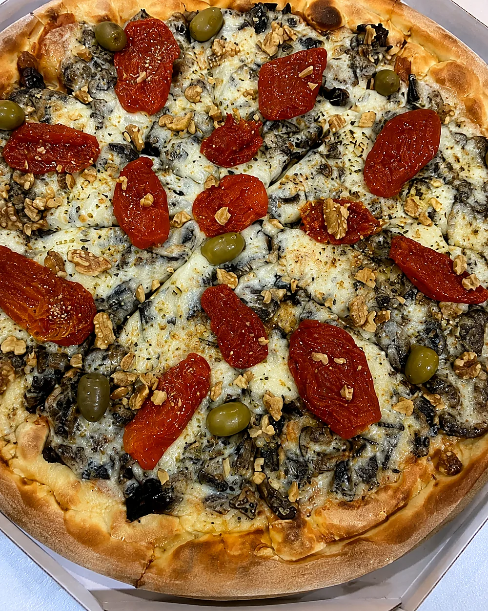 Pizza com tomate seco, nozes e azeitonas preparada pela Pizzaria Recanto Novo